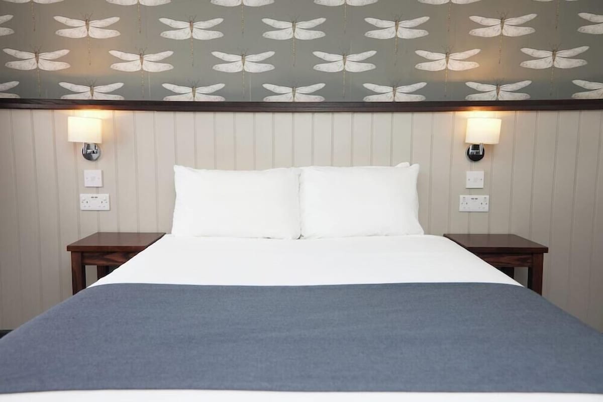 Une chambre d’hôtel avec un lit, deux tables de chevet et des lampes fixées au mur.