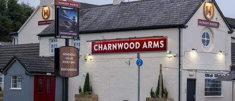A building with a sign reading "CHARNWOOD ARMS" and a smaller sign below stating "GENUINE VALUE EVERY DAY BEER GARDEN".