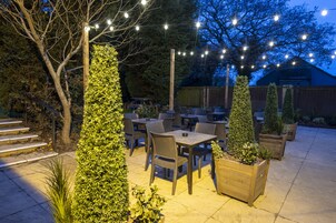 Un patio al aire libre con mesas y sillas, rodeado de follaje y árboles.