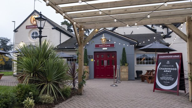 A building with a red door labeled "WELCOME" and a signboard for "CHARNWOOD ARMS". - Charnwood Arms by Greene King Inns (Coalville)