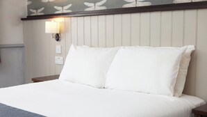 A neatly made bed with white linens and a blue throw blanket, a wall-mounted lamp, and a power outlet on the wall. - Charnwood Arms by Greene King Inns (Coalville)