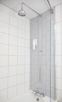 Un baño moderno con azulejos blancos, cerramiento de ducha de vidrio, ducha de mano y dispensador de jabón.