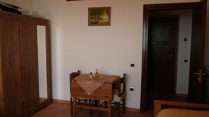 A room with a wooden cabinet, a dining table with chairs, a painting on the wall, and a door. - Il Rifugio del Poeta (Ravello)