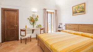A bedroom with a wooden bed, a desk with a chair, a small table with a vase of flowers, and a door. - Il Rifugio del Poeta (Ravello)