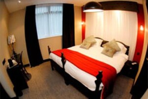 Una camera d'albergo con un letto grande, un comodino, una lampada e una finestra con tende.