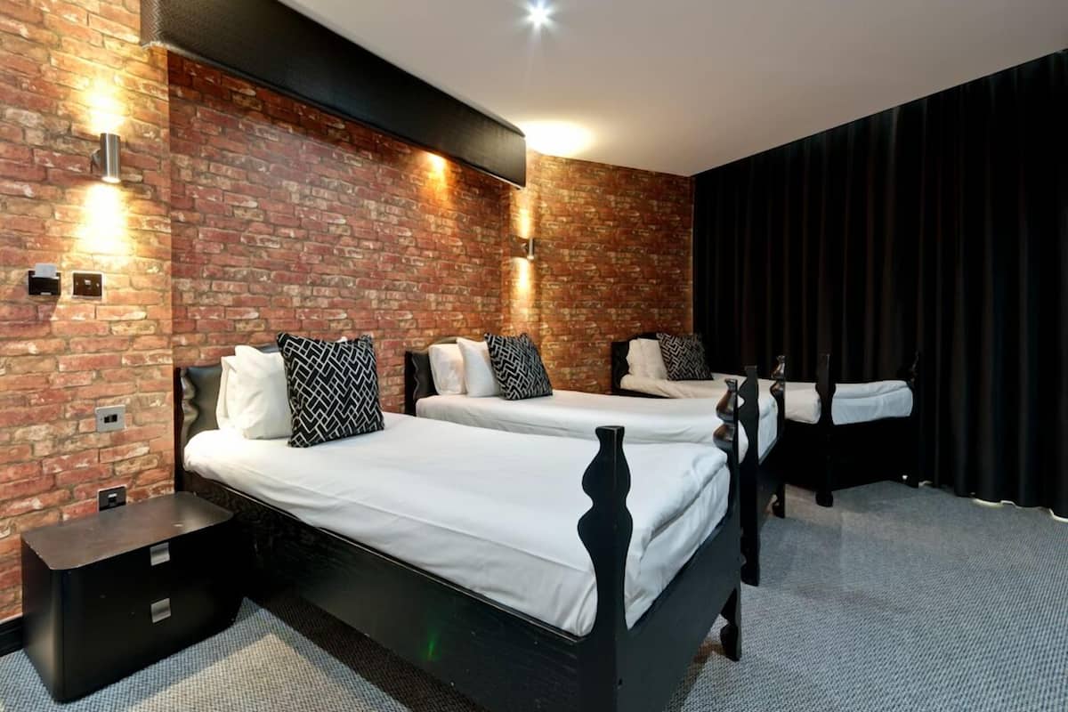 Hotellihuone, jossa on kaksi sänkyä, tiiliseinä ja moderni valaistus.