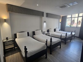 Habitación de hotel con tres camas individuales, una mesita y ventana con vistas al exterior.
