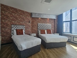 Habitación de hotel con dos camas, pared de ladrillo, ventana grande y diseño de techo moderno.