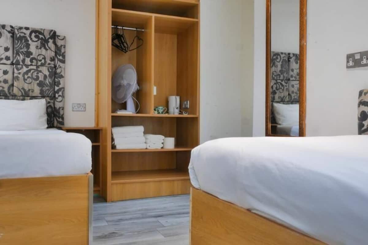 Hotellihuone, jossa on kaksi sänkyä, puinen vaatekaappi ja peili.