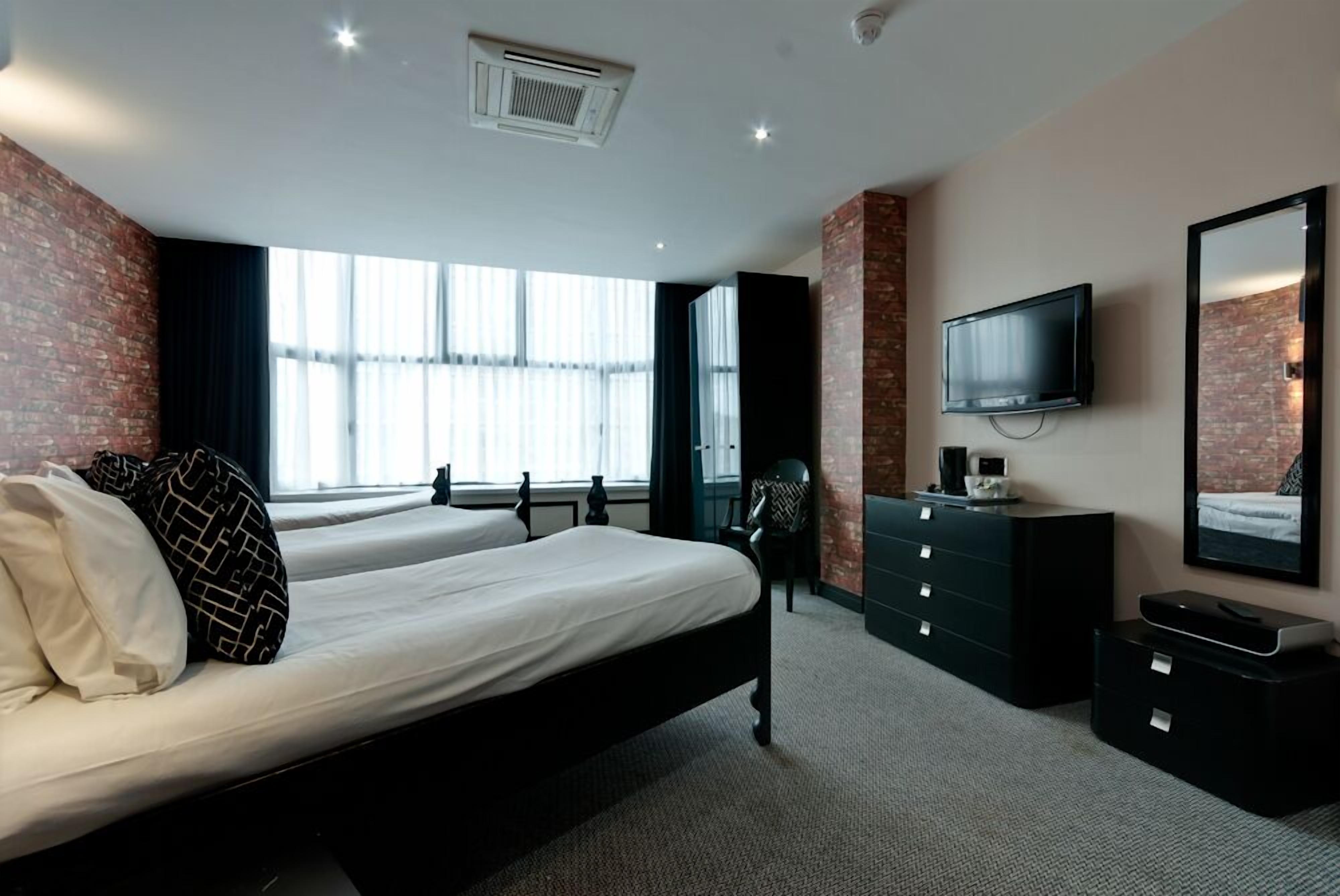 A modern hotel room with two beds, a TV, a dresser, and a large window with curtains.