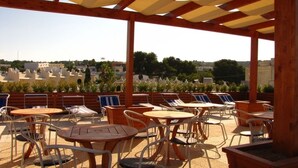 An outdoor patio area with tables and chairs, wooden pergola, and a view of buildings in the background.