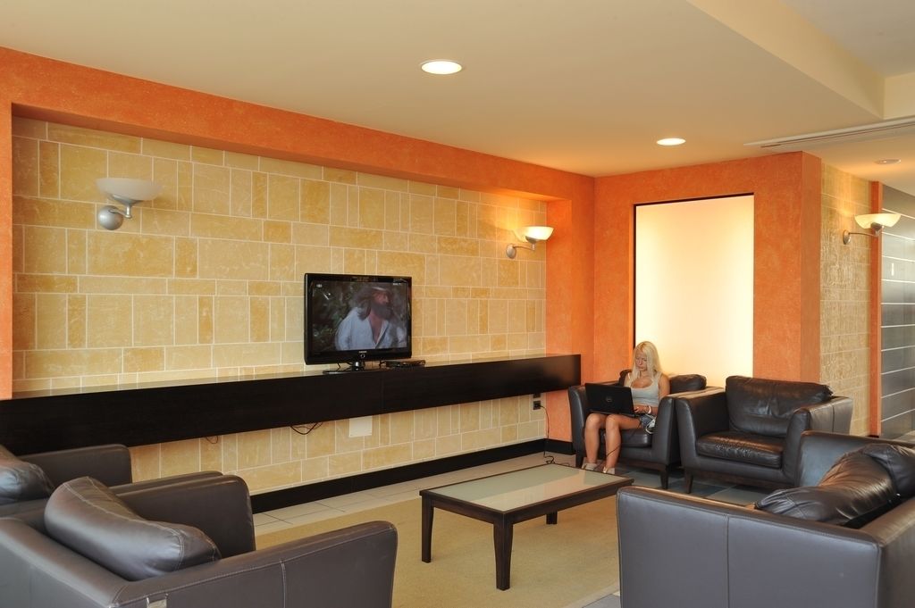 Un hall d’entrée avec un téléviseur fixé au mur, des canapés en cuir noir et un mur recouvert de carreaux avec des touches de couleur orange.