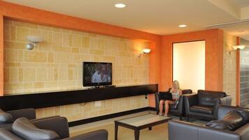 Un hall d’entrée avec un téléviseur fixé au mur, des canapés en cuir noir et un mur recouvert de carreaux avec des touches de couleur orange.