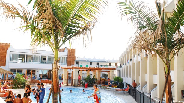 A pool area with palm trees, lounge chairs, and a building with multiple floors and balconies.