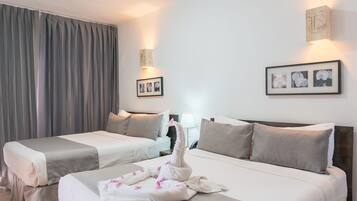 A hotel room with two beds, a large window with curtains, a wall-mounted light, and framed pictures.