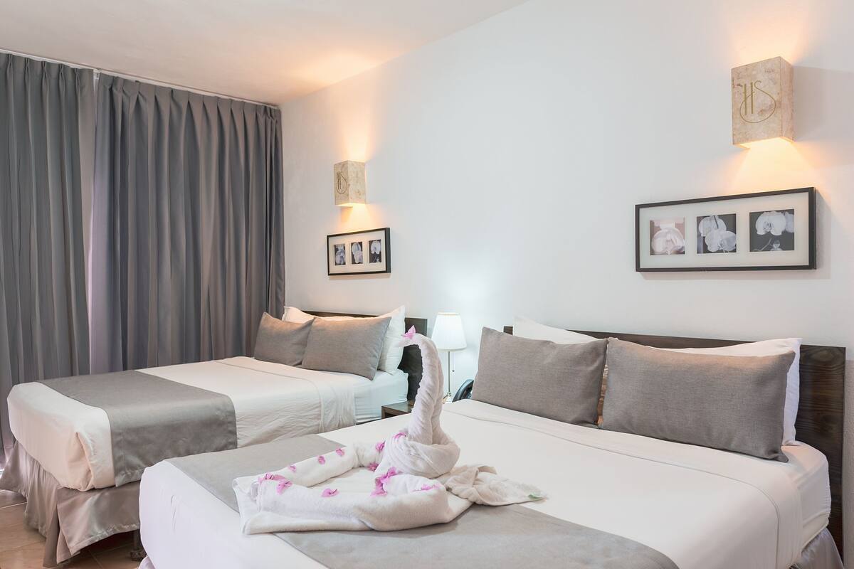 Habitación de hotel con dos camas, un ventanal con cortinas, una lámpara de pared y un cuadro enmarcado.