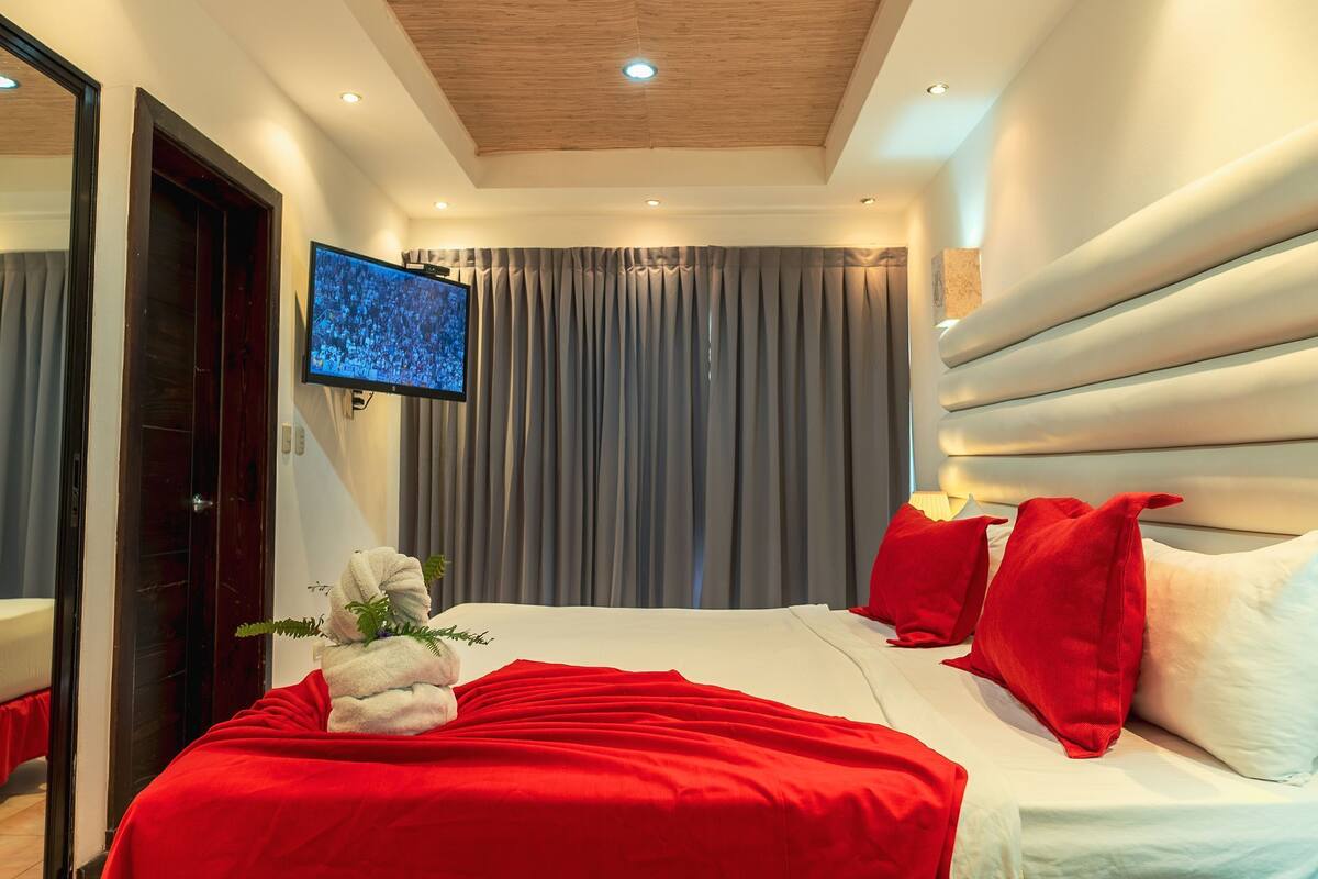 Una habitación de hotel con una cama, televisión, cortina y cabecero.