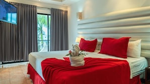 A modern hotel room with a large bed, red bedding, a TV on the wall, and a balcony with curtains.
