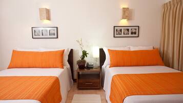 A hotel room with two beds, each with an orange bedspread, a nightstand with a lamp and a plant, and framed pictures on the walls.