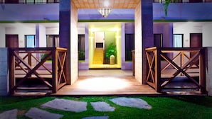 A hotel entrance with a wooden gate, a staircase leading to the second floor, and a well-maintained lawn.