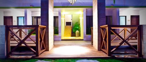 A hotel entrance with a wooden gate, a staircase leading to the second floor, and a well-maintained lawn.