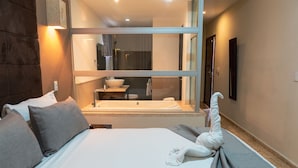 A hotel room with a large bed, a bathroom with a sink and mirror, and a towel on the bed.