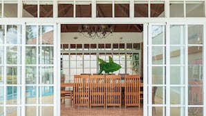 A dining area with a wooden table and chairs, large windows, and a chandelier.