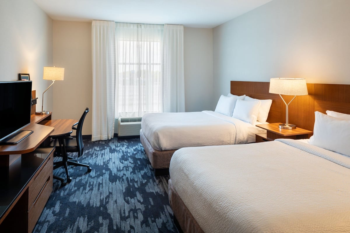 A hotel room with two beds, a desk with a chair, a TV, and a window with curtains.