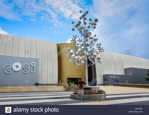 A modern building with a large 'COSI' sign, a unique metallic sculpture resembling a tree, and a 'WESU' sign.