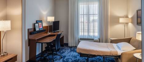 A hotel room with a bed, a desk with a computer, a chair, a sofa, and a window with curtains.