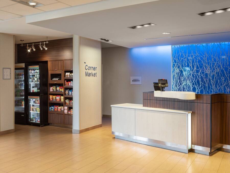 A reception area with a 'Corner Market' sign, a refrigerator stocked with beverages, and a blue abstract wall.