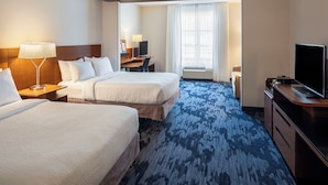 A hotel room with two beds, a desk, a television, and a large window with curtains.