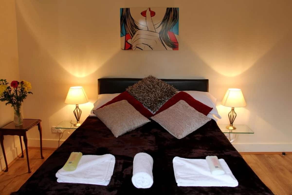 A hotel room with a large bed, two bedside lamps, a painting on the wall, and a vase with flowers on a side table.