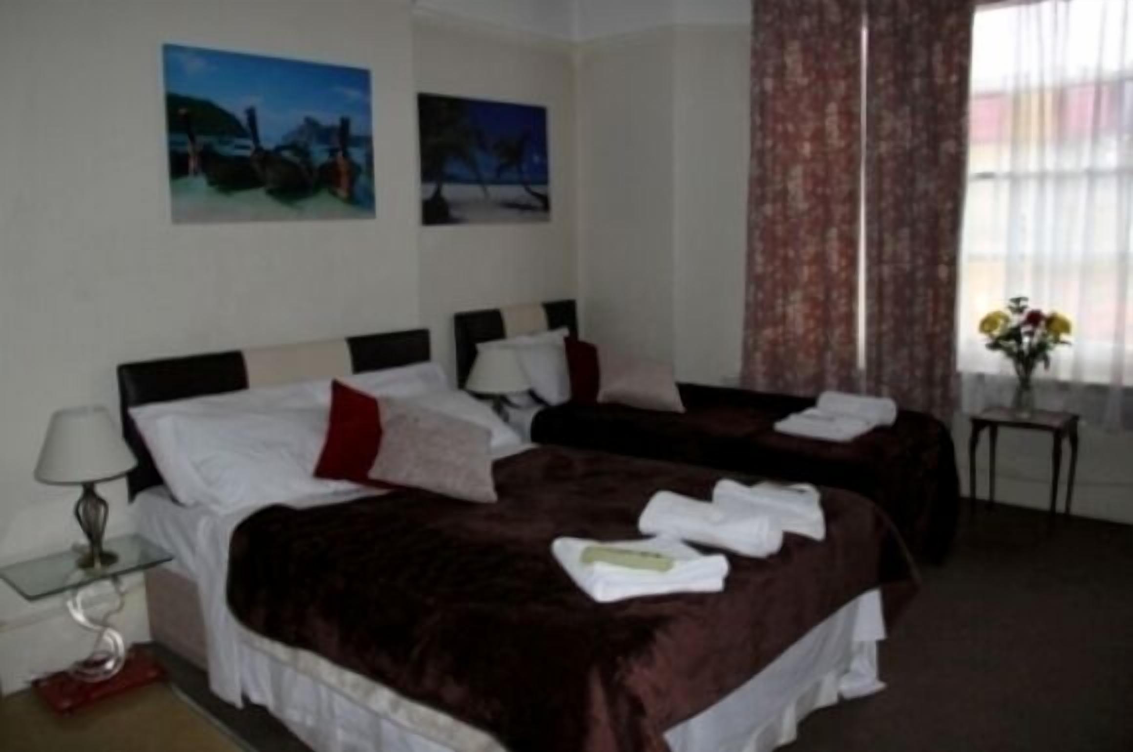 Ein Hotelzimmer mit zwei Einzelbetten, einem kleinen Tisch mit Lampe und zwei Bildern an der Wand.