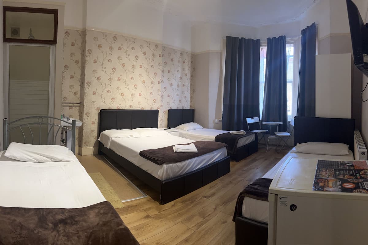A hotel room with two single beds, a double bed, a small table, a chair, a TV, and a refrigerator.