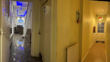 Un couloir d’hôtel avec un sol en marbre, une porte réservée au personnel, un extincteur et un radiateur.
