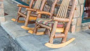 Three wooden rocking chairs with cushioned seats and backs, placed on a concrete ledge outside a building with a stone wall. - Mountain Breeze Motel (Pigeon Forge)