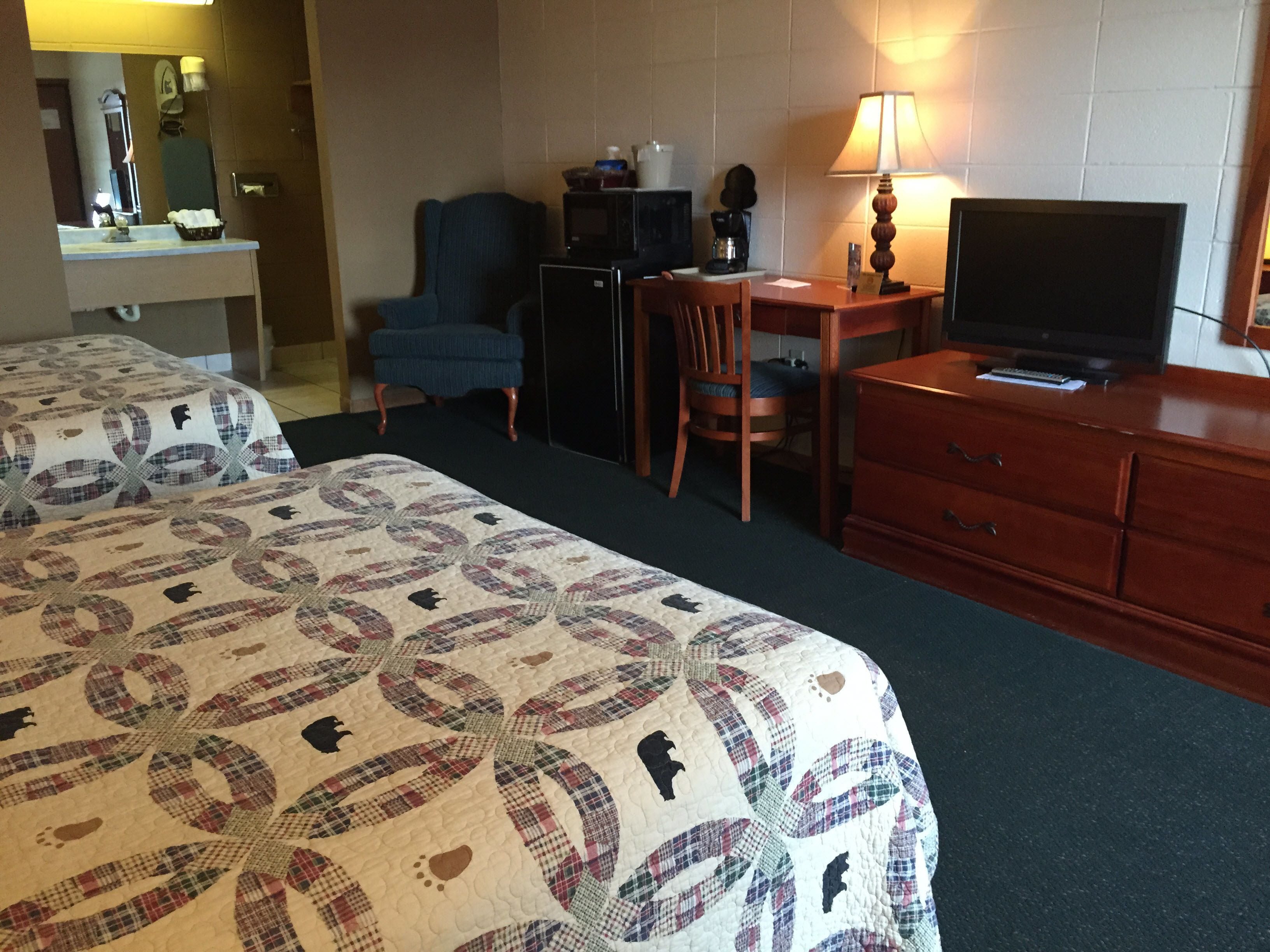 A hotel room with two beds, a desk with a computer, a television, and a lamp.