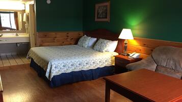 A hotel room with a bed, bedside table, lamp, and a small table.
