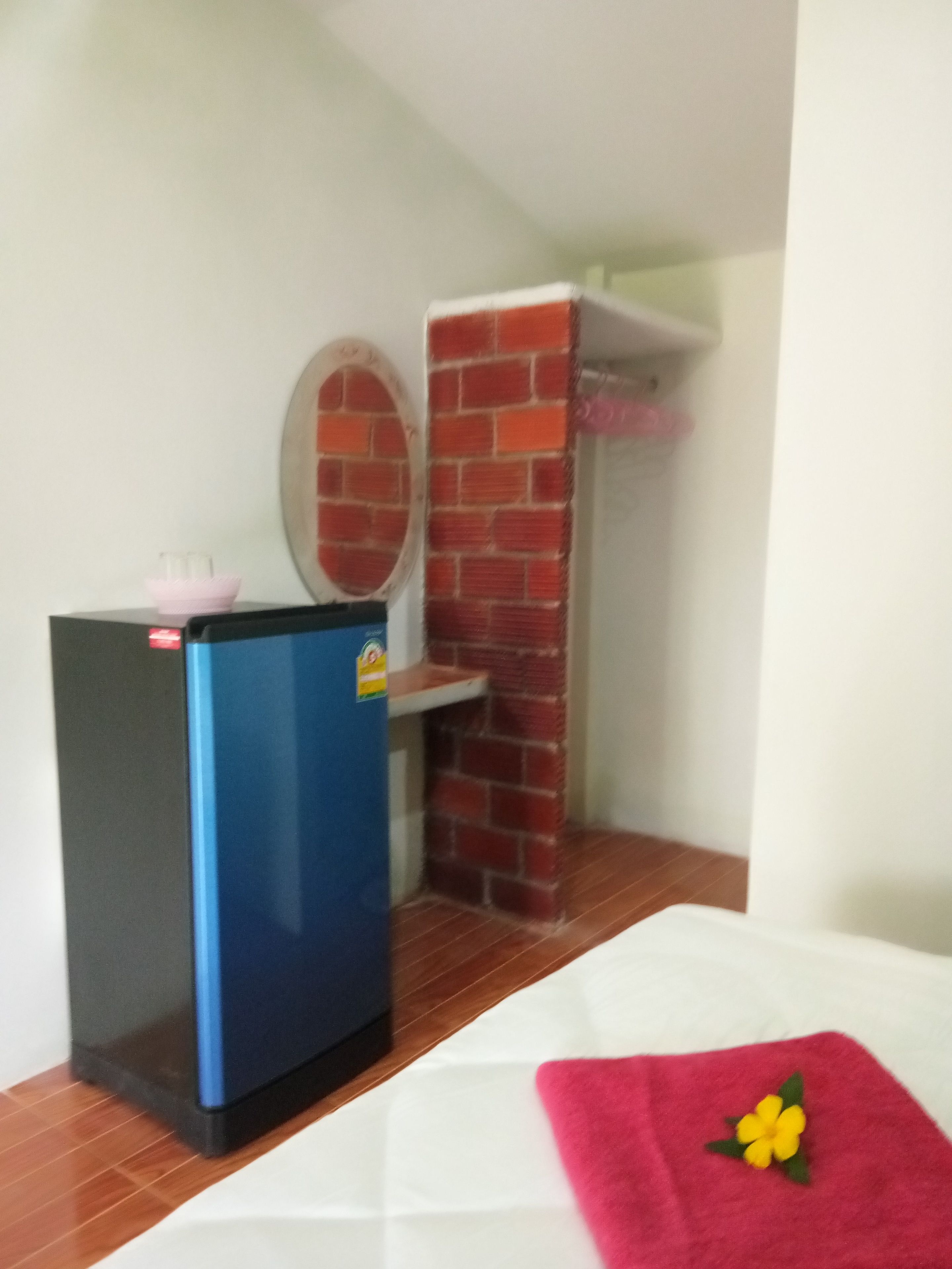 A compact room with a small blue refrigerator, a pink flower on a white towel, and a brick wall.