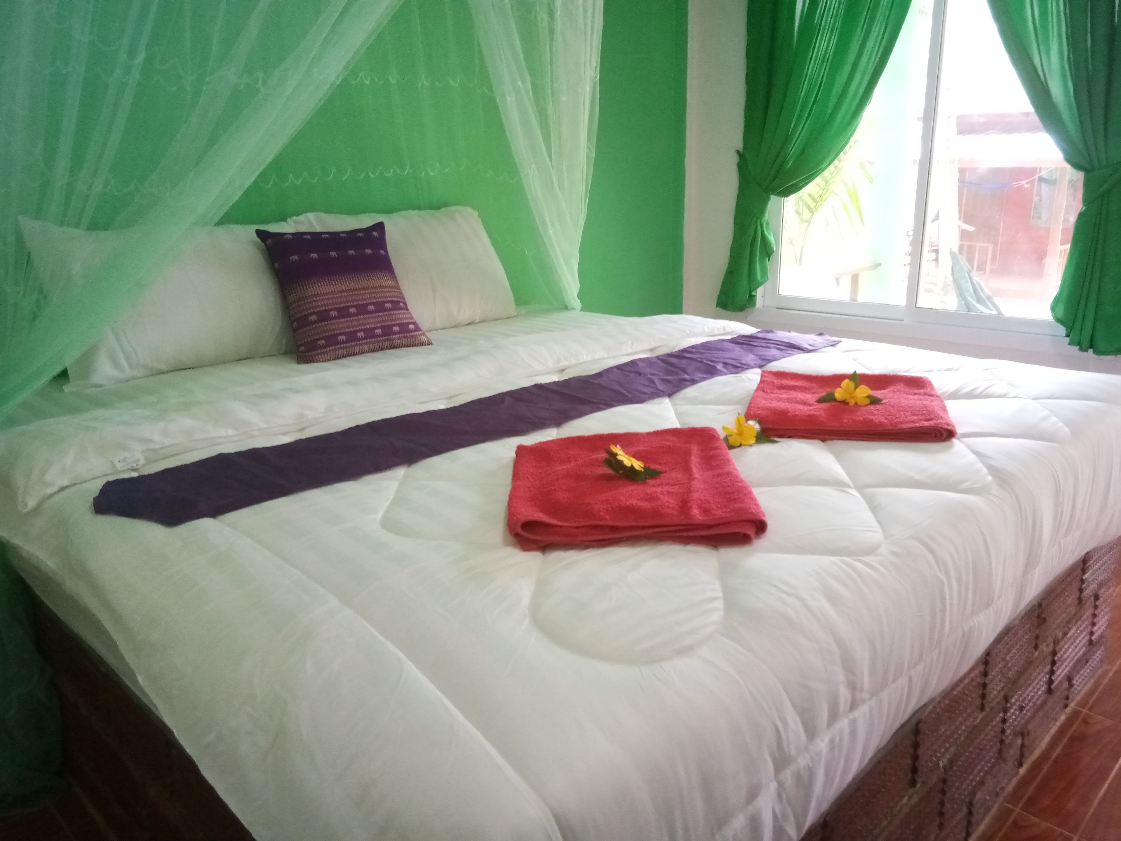 A bed with white bedding, green curtains, and a purple bedspread.