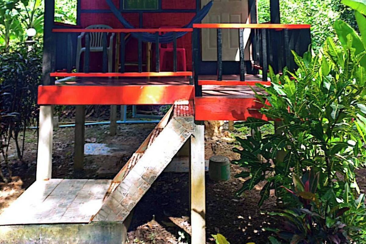 Une petite construction rouge, d’un seul étage, avec un toit en tuiles, un escalier en bois et un banc.