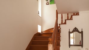 Un escalier en bois avec une rampe, un miroir fixé au mur et une petite table sur laquelle se trouvent un vase et une plante.