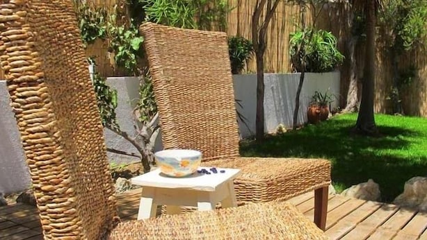 Une chaise en osier, avec une petite table, un bol et une tasse posés sur la table.