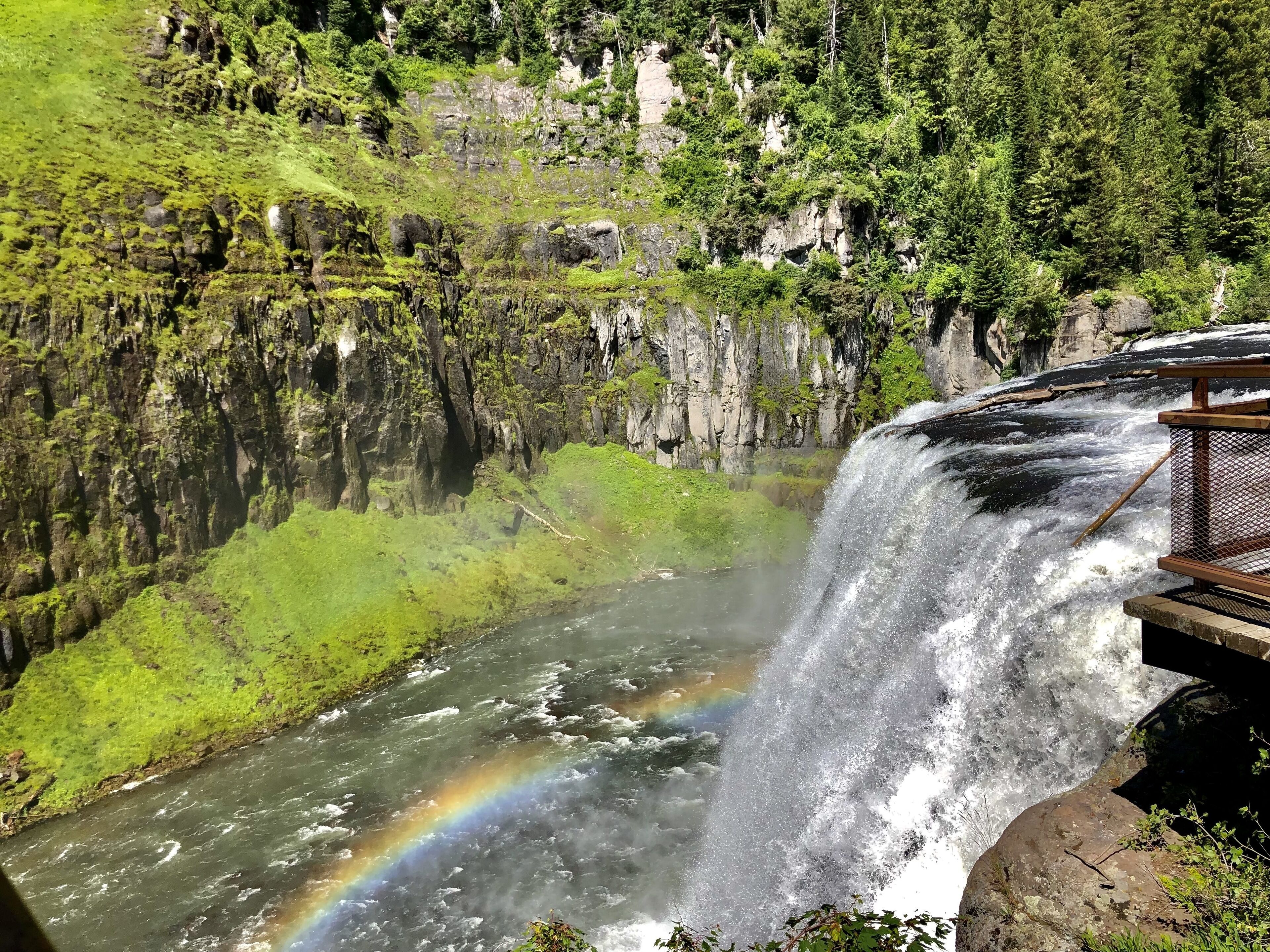 Una cascada con un arcoíris, rodeada de exuberante vegetación y escarpados acantilados.
