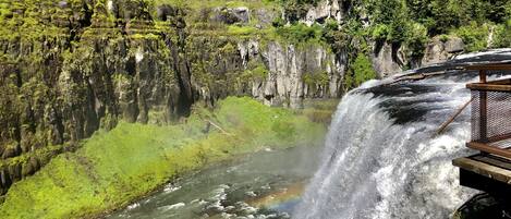 Una cascada con un arcoíris, rodeada de exuberante vegetación y escarpados acantilados.