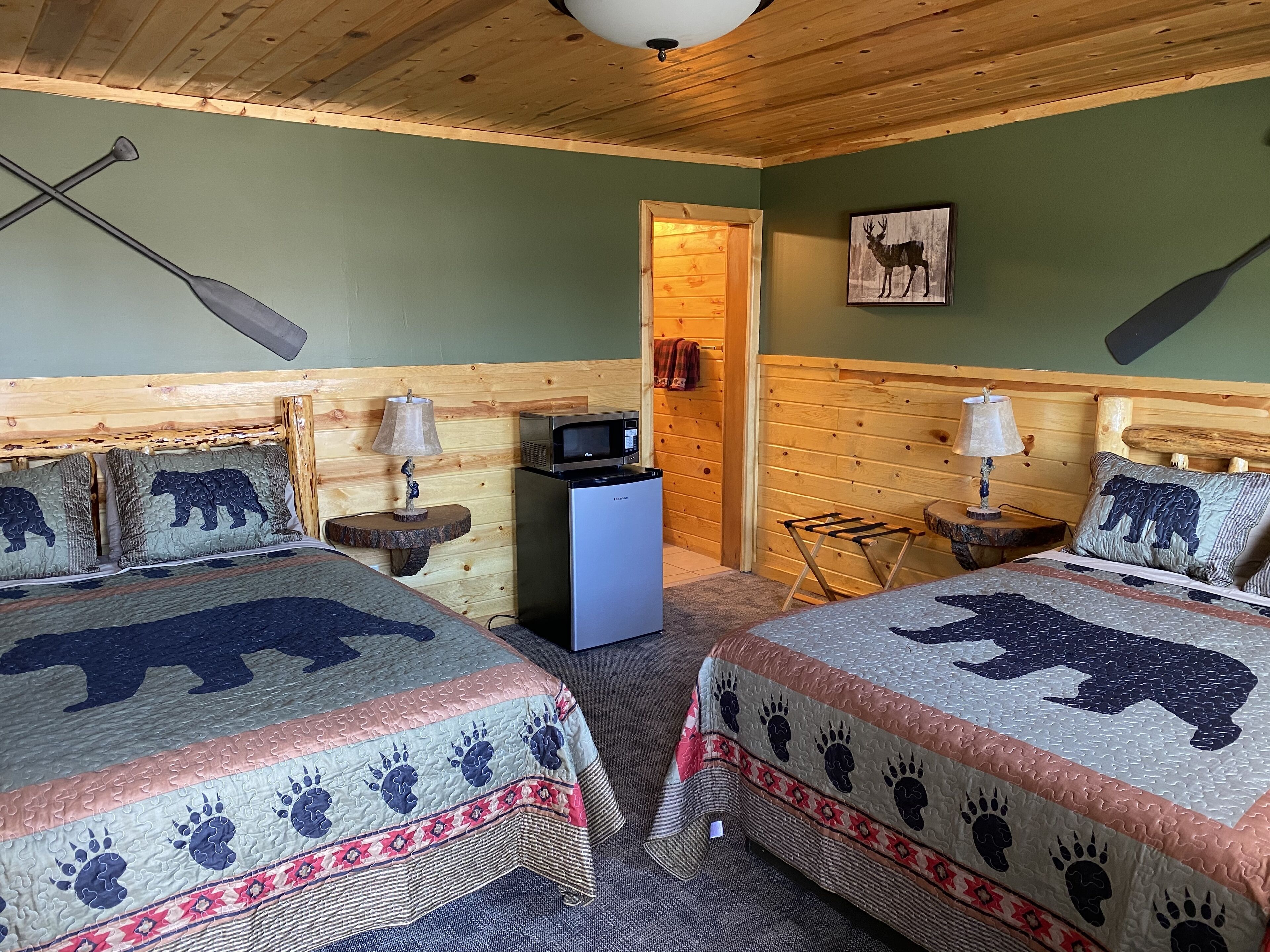 Una habitación acogedora con dos camas, ropa de cama con motivos de osos, techo de madera y una pequeña kitchenette.