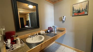 Ein Badezimmer mit einem Holzkosmetikschrank, einem Waschbecken, einem Spiegel, einem Händetrockner und einem Bild von einem Kanu an einem Baum.
