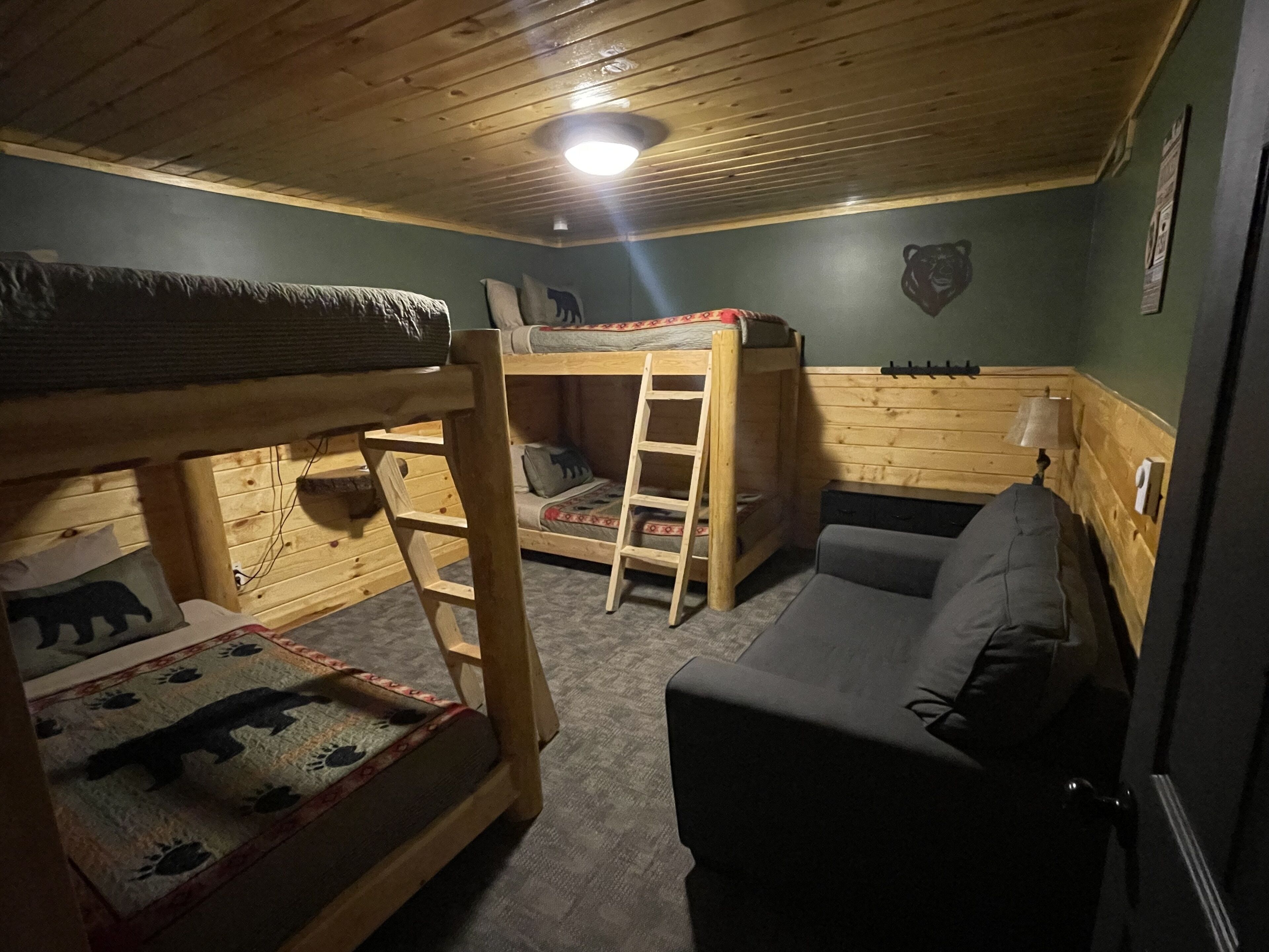 Una cama litera con escalera, un sofá y una estantería de pared con libros.