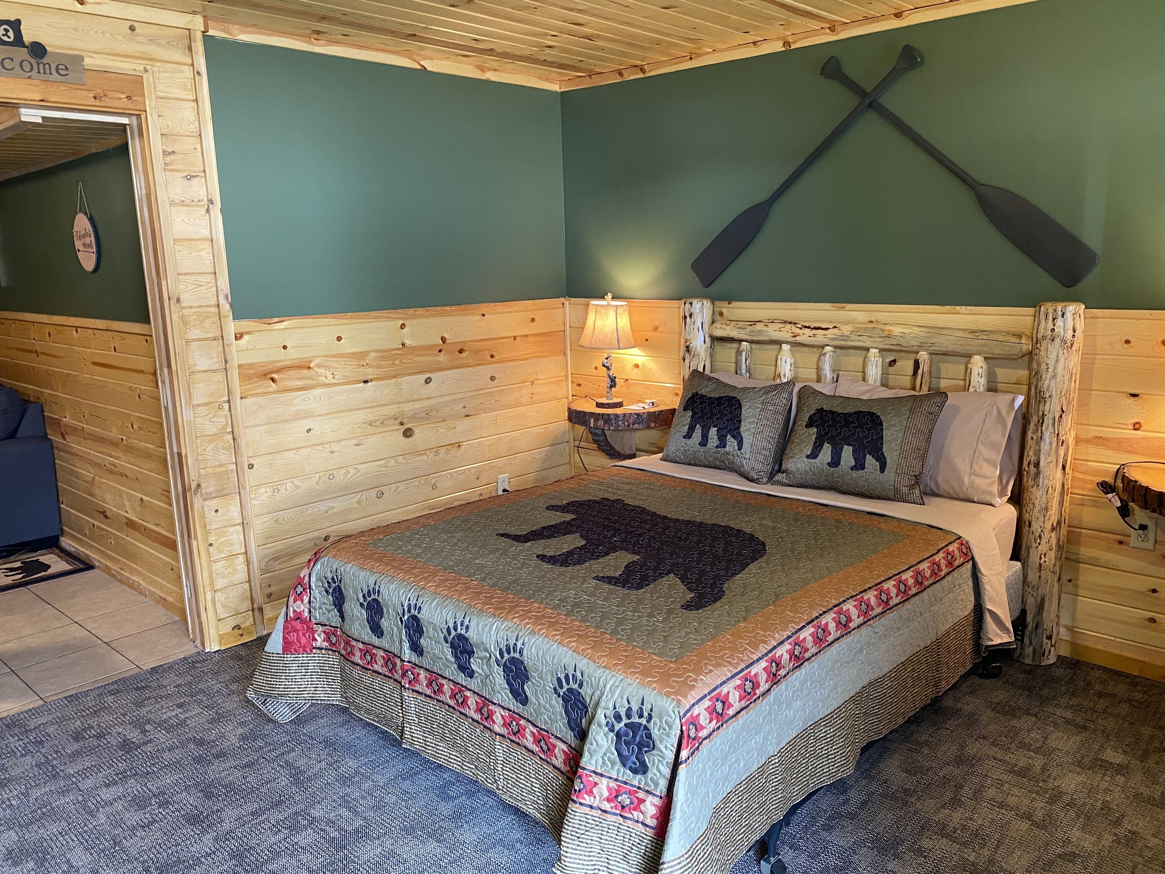 Habitación con paneles de madera, una cama, una mesita de noche y un remo colgado en la pared.